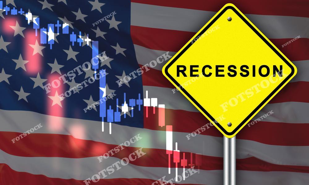 На изображении желтый знак с надписью "Recession" на фоне американского флага и свечного графика с падающими показателями. Фотография символизирует рецессию, вызовы для экономики США и глобальные финансовые трудности.